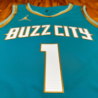 Regata City Edition Charlotte Hornets Jordan 2023/24 Azul e Dourada - Inspirada na história dourada de Charlotte, com design azul-petróleo, detalhes em menta e dourado. Logotipos primários em ouro, branco e azul. Painéis laterais menta lembrando uma colmeia, emblema de vespas douradas nos shorts e a frase "The Hive is Alive" no jocktag.